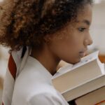 Side profile of a thoughtful young woman with afro hair holding books, symbolizing knowledge and education.